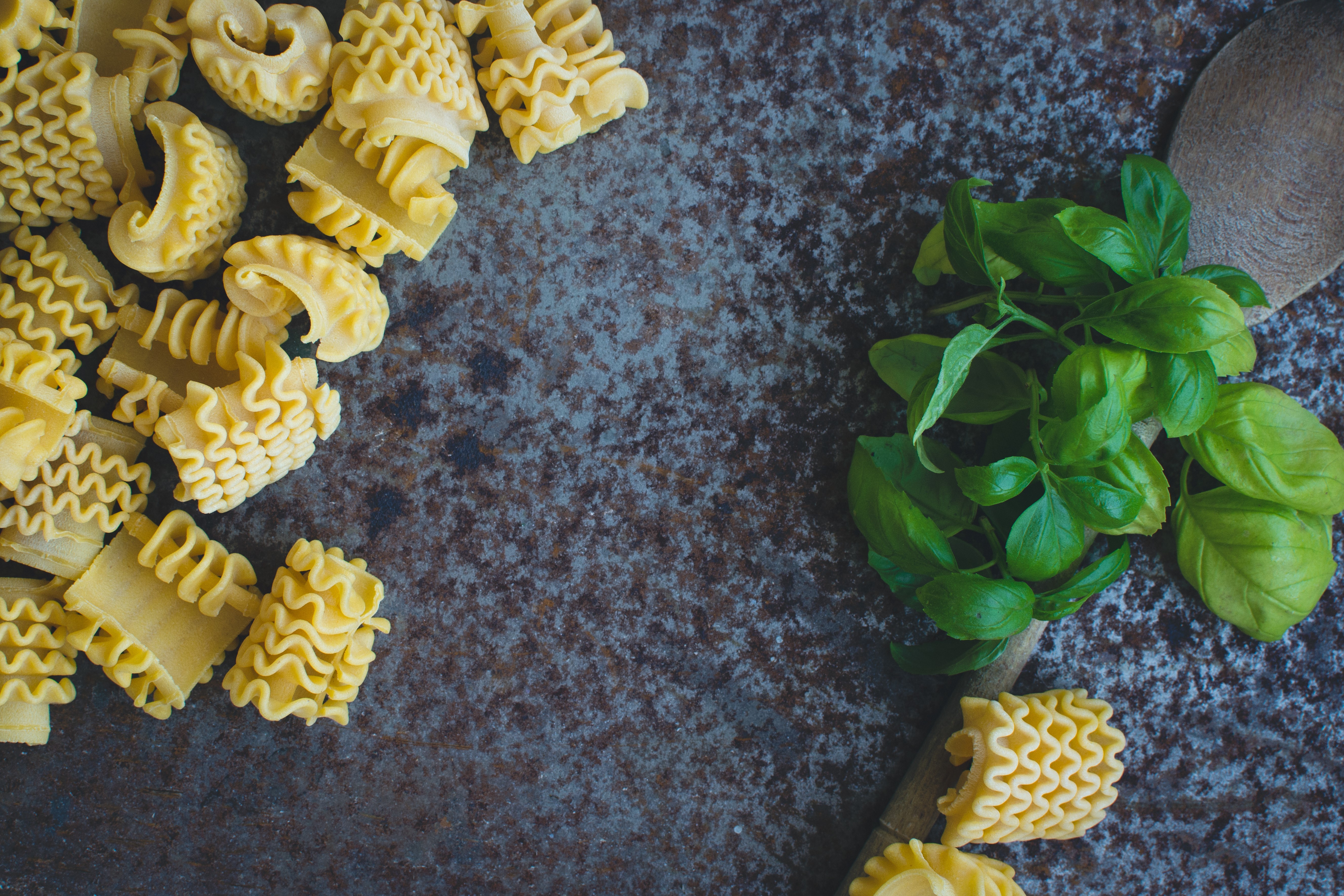 Pasta con albahaca y cuchara de madera sobre un fondo metálico oxidado